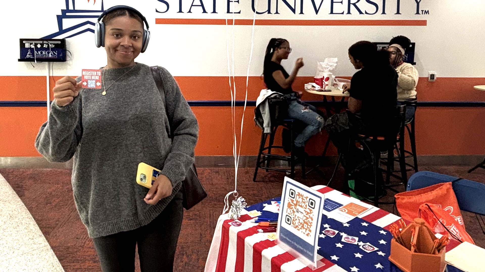 female student holding up a register to vote here signage