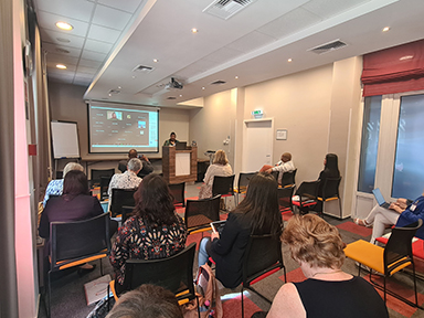 This image shows a group of people seated in a conference room, facing a speaker who appears to be giving a presentation. The setting looks formal and professional, consistent with an academic or business event.