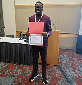 This image shows a person standing in a conference or formal meeting room, holding a certificate or document and posing for a photograph.