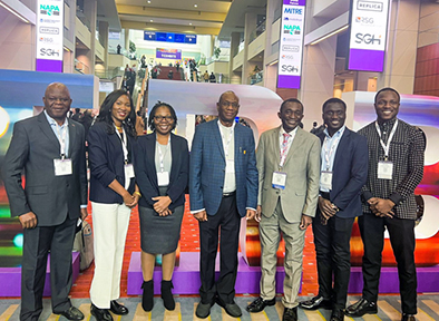 This image shows a group of seven people standing together in what appears to be the lobby or common area of a conference or event venue. The setting is modern, with a vibrant and professional atmosphere.